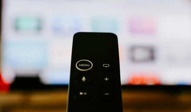 Apple TV remote pointing to a tv, with a blur screen showing thumbnails of apps