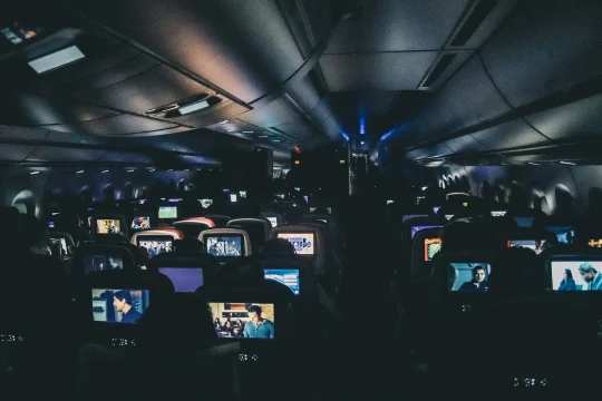 Passengers on a nighttime flight watching movies on seatback screens, illustrating modern in-flight entertainment systems powered by streaming technology and connected content delivery.