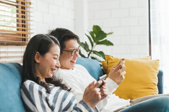two people sitting on a couch while watching their phones and laughing